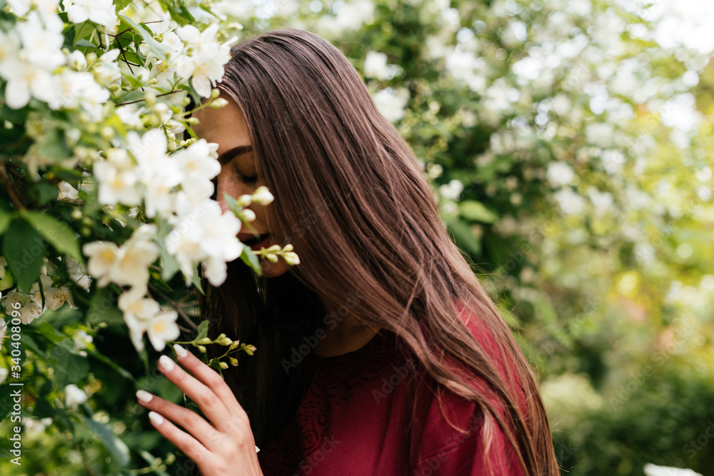 romantic long-haired brunette in a cherry-colored dress buried her face in jasmine flowers and gently covering her eyes enjoys the aroma romantic long-haired brunette in a cherry-colored dress buried her face in jasmine flowers and gently covering her eyes enjoys the aroma
