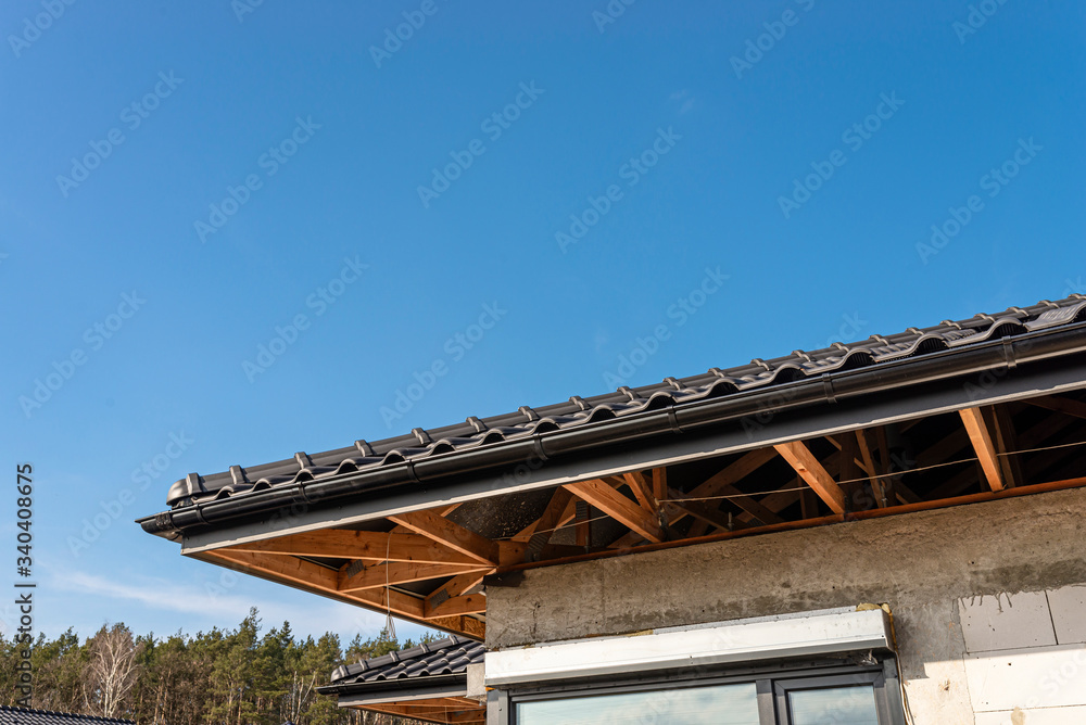 The roof of a single-family house covered with a new ceramic tile in anthracite against the blue sky, visible trusses.
