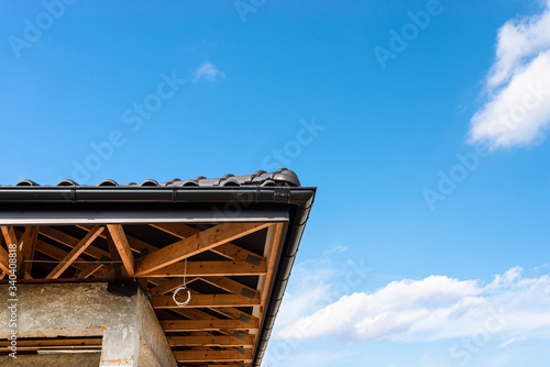 The roof of a single-family house covered with a new ceramic tile in anthracite against the blue sky, visible trusses. 