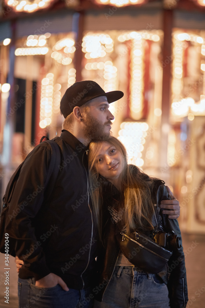 young couple hugging in front of carousel during night. man and woman love merry-go-round 