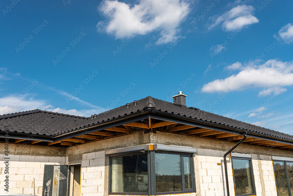 The roof of a single-family house covered with a new ceramic tile in anthracite against the blue sky, visible trusses.
