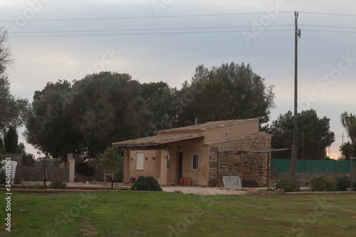 Small house at a natural rural field. Yard with wooden fence and plants. photo