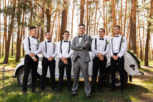 Group wedding photo of elegant groom in grey suit and groomsmen with black bow ties and suspender at wedding day photo