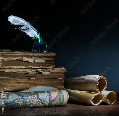 Quill pen, inkwell, old rolled up maps and papers on a dark background