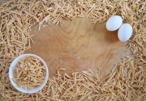 Russian traditional homemade noodles on a wooden background with copy space, some noodles in a bowl and two white eggs