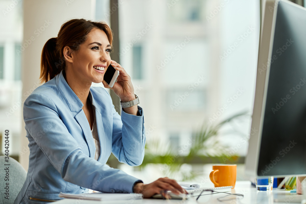 Happy businesswoman talking on the phone while using computer in the office. Happy businesswoman talking on the phone while using computer in the office.