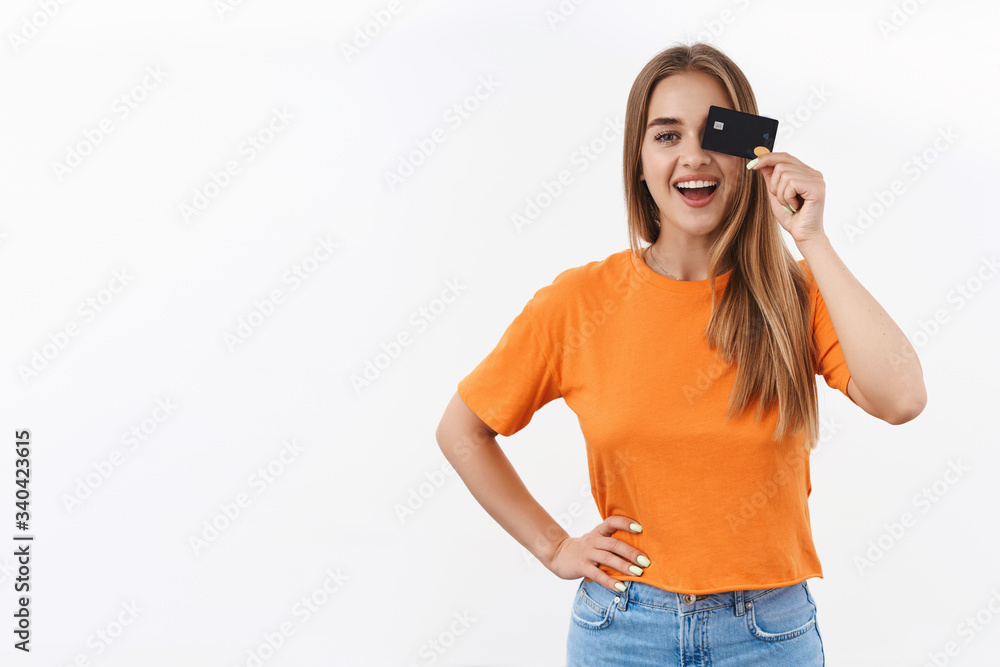 Portrait of cheerful blond girl in orange t-shirt, sitting at home likes shop online, buying new clothes for summer after self-quarantine lockdown, hold credit card over eye and smiling pleased Portrait of cheerful blond girl in orange t-shirt, sitting at home likes shop online, buying new clothes for summer after self-quarantine lockdown, hold credit card over eye and smiling pleased