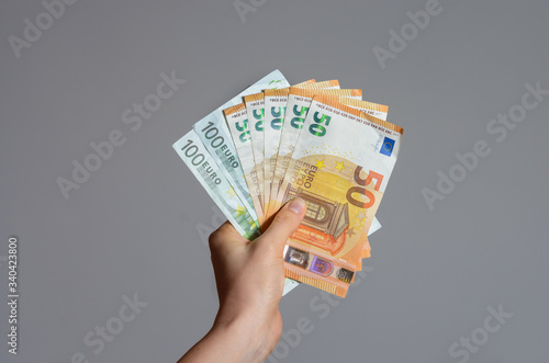 Close up view of a woman's hand holding a pile of euro banknotes   money on a gray background . The economic impact of coronavirus  in  European Union .