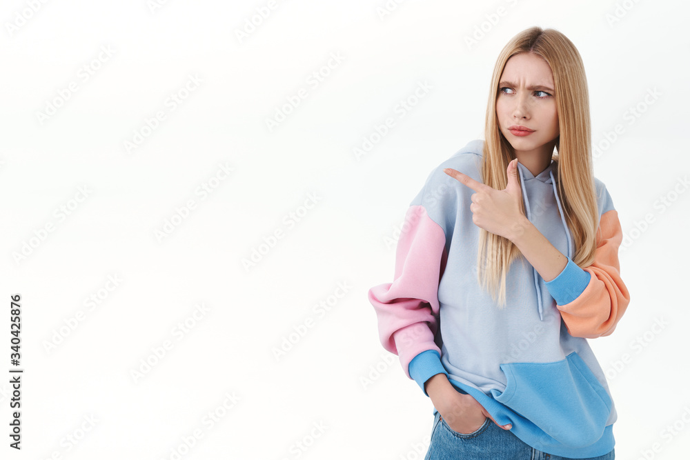 Portrait of doubtful, suspicious blonde girlfriend having hesitation, squinting and frownign skeptical, looking pointing finger left with judgement and disappointment, dont like product Portrait of doubtful, suspicious blonde girlfriend having hesitation, squinting and frownign skeptical, looking pointing finger left with judgement and disappointment, dont like product