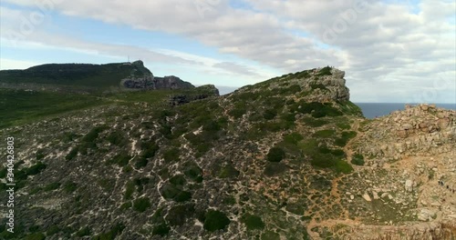 Aerial shot of people climbing to lookout point on mountain peak over scenic cove, drone flying forward passing over the peak showing the cove - Cape Town, South Africa photo