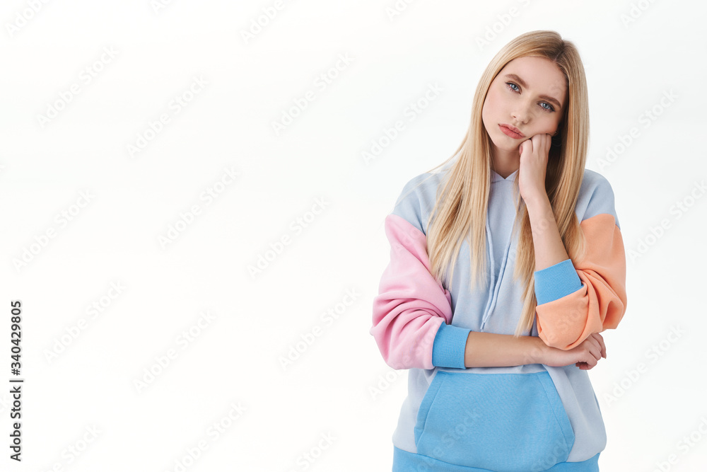 Bored in house. Portrait of indifferent moody teenage blond girl, wear hoodie, lean on arm and staring with uninterested expression camera, feeling pensive, watching boring movie Bored in house. Portrait of indifferent moody teenage blond girl, wear hoodie, lean on arm and staring with uninterested expression camera, feeling pensive, watching boring movie