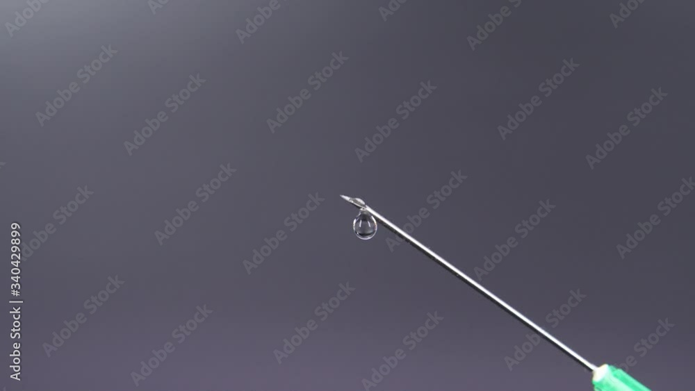 A syringe needle releases a drop of clear liquid A syringe needle releases a drop of clear liquid