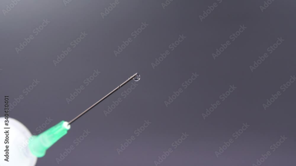 A syringe needle releases a drop of clear liquid A syringe needle releases a drop of clear liquid