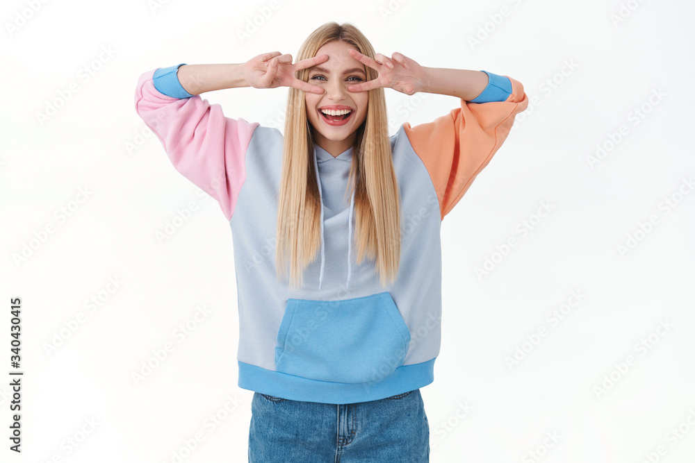 Enthusiastic attractive young girl in hoodie, showing peace signs over eyes, laughing and smiling, express happiness and joy of summer holidays, feeling rejoice, white background Enthusiastic attractive young girl in hoodie, showing peace signs over eyes, laughing and smiling, express happiness and joy of summer holidays, feeling rejoice, white background