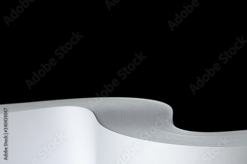 Studio photo of multiple sheets of rolled A4 paper stack (S-shaped ream) on black background. Simple, isolated object with copy space perfect for illustrating various concepts. Selective focus (shallo