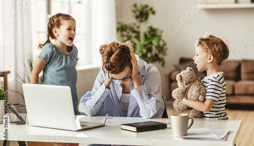 Little naughty children distracting busy young woman from work on laptop at home
