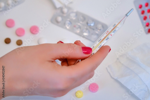 A woman s hand holds a thermometer over a table with pills  concept
