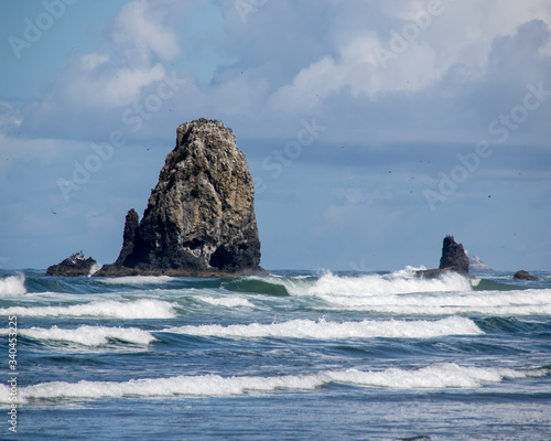 Surf rolling onto beach past rocky bluffs under a blue-gray sky with cumulus clouds