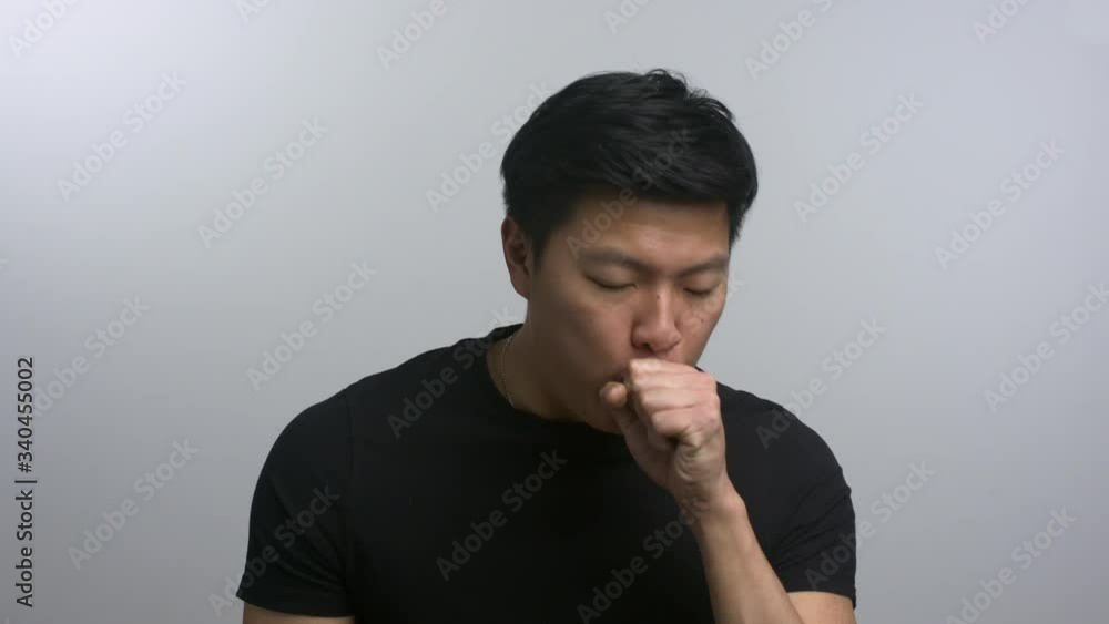 Casually dressed Asian man coughing into hand