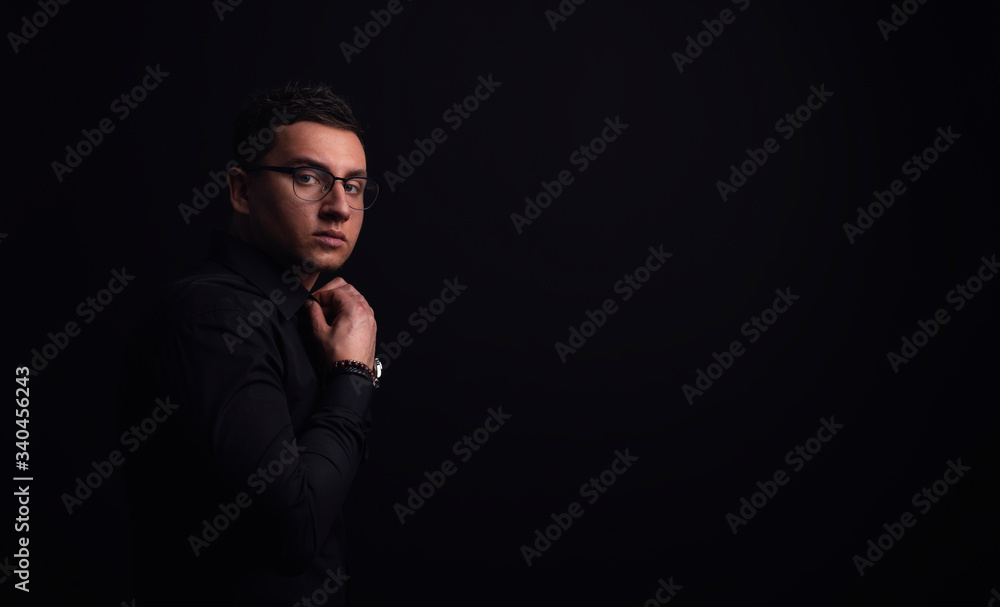 Handsome young man on black background looking at camera. Portrait of Handsome man buttoning shirt against grey wall