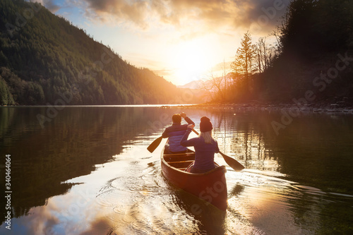 Fototapeta Couple friends canoeing on a wooden canoe during a colorful sunny sunset