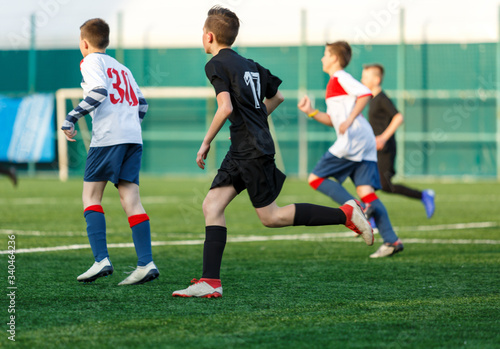 Boys in white black sportswear running on soccer field. Young footballers dribble and kick football ball in game. Training, active lifestyle, sport, children activity concept © Natali