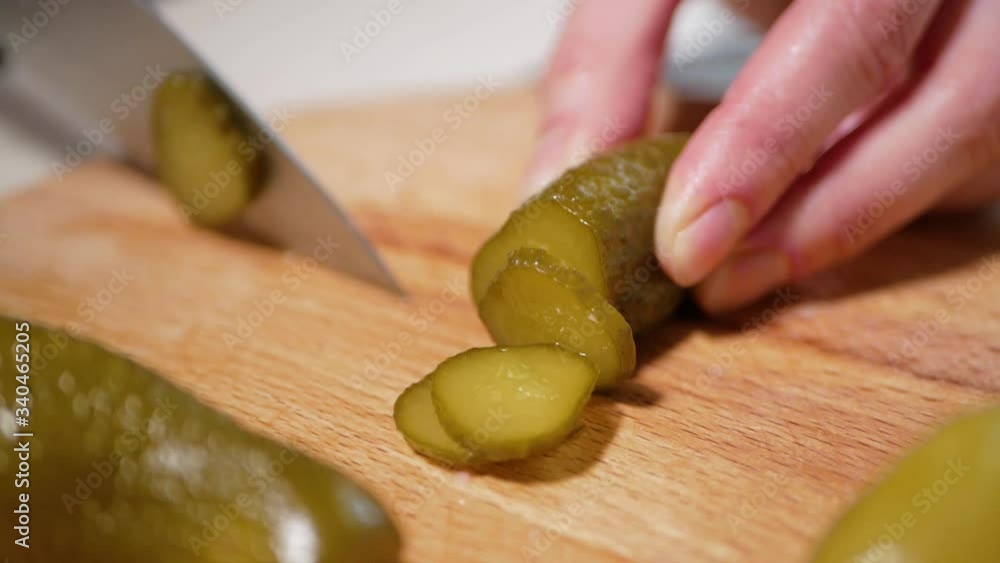 Young woman cuts the pickled cucumbers on a wooden cutting board, close-up Young woman cuts the pickled cucumbers on a wooden cutting board, close-up