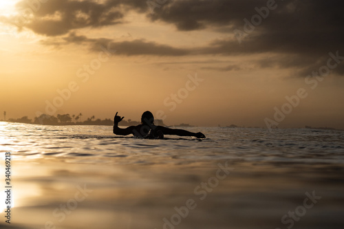 silhouette of man surfing at sunset in the ocean with shaka