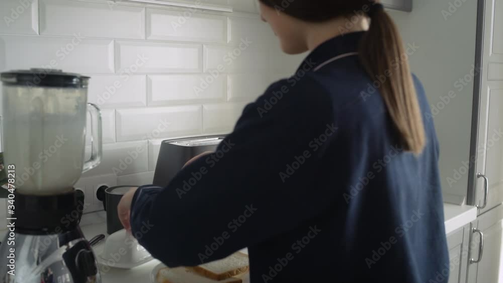 Young woman in black pajamas preparing breakfast at the morning. Woman spreads butter on roasted bread Young woman in black pajamas preparing breakfast at the morning. Woman spreads butter on roasted bread