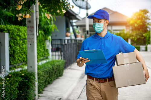 Asian delivery man in blue t-shirt carrying parcel box and document to sign in front of customer home. Delivery man concept.