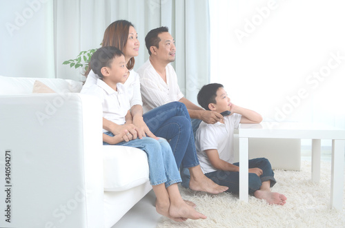 Asian happy family sitting and watching television at home. Social Distancing, stay at home, holiday or lifestyle concept.