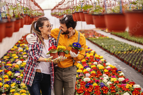 Two nursery garden workers holding pots with flowers and hugging. All around are all sorts of colorful flowers. © dusanpetkovic1