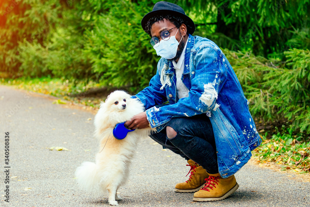 afro man in mask hugging his fluffy spitz in park afro man in mask hugging his fluffy spitz in park