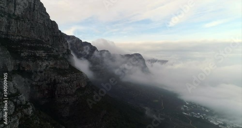 Aerial shot of an amazing mountain peak among clouds over scenic town, drone flying forward - Cape Town, South Africa photo