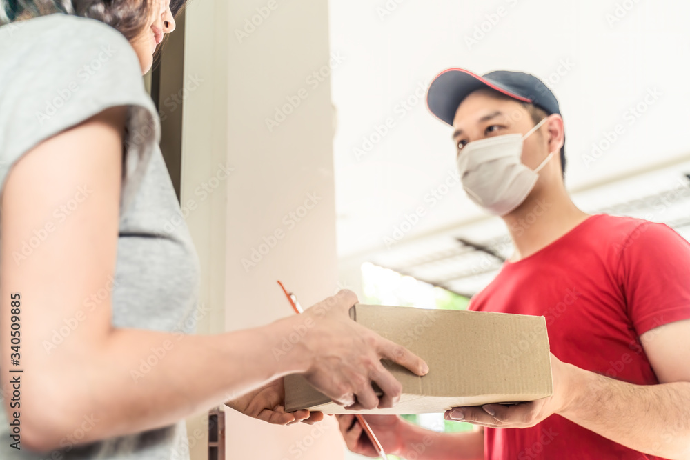 Fototapeta premium Asian postman or deliveryman carry small box deliver to young woman customer in front of door at home. Man wearing mask prevent covid or coranavirus affection outbreak. Social distancing work concept.