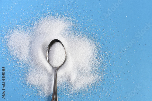 Bilde på lerret A top view image of a metal spoon and white sugar on a bright blue background
