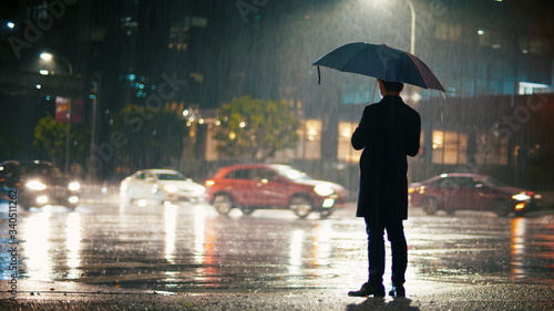 On a rainy night, a man with an umbrella stands on the city street, coronavirus