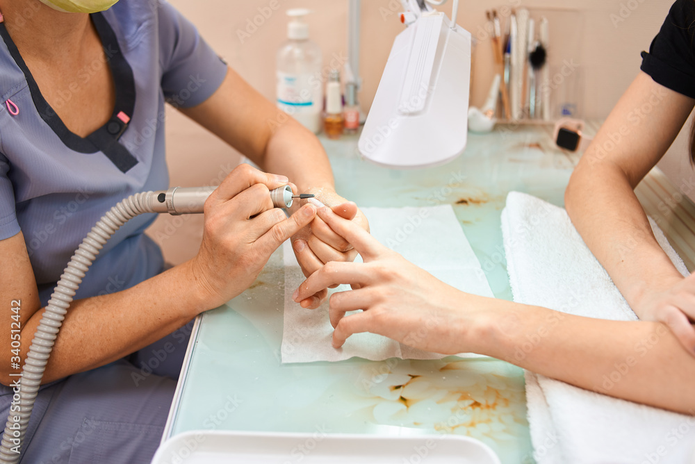 Fototapeta premium woman master manicures a girl. Removes varnish with a cutter. process
