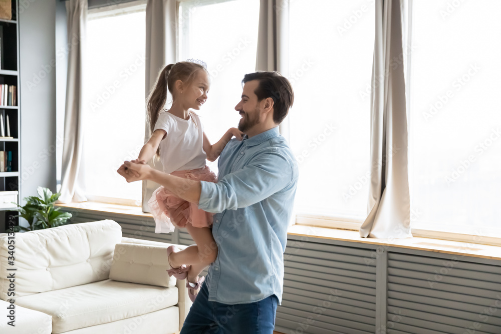 Loving dad holds on hands small daughter she wears crown imagines herself like princess, people dancing in living room, enjoy holiday life event birthday party. Happy fatherhood, family bonds concept