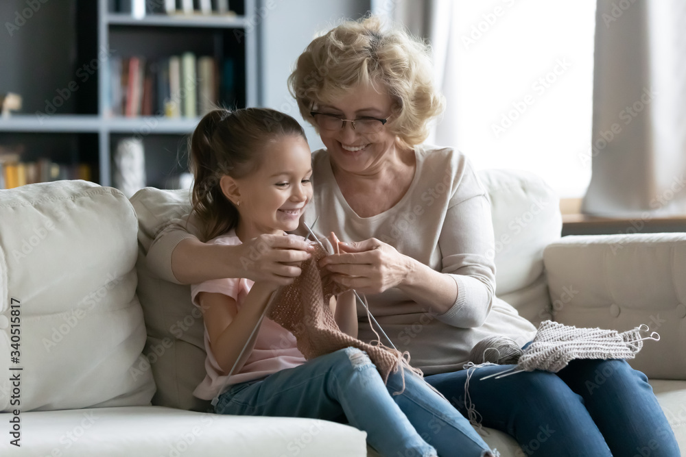 Senior grandmother teaches little granddaughter to knit seated on couch, multi generational people loving family holding needles and yarn, hobby and fun, activity to improve fine motor skills concept Senior grandmother teaches little granddaughter to knit seated on couch, multi generational people loving family holding needles and yarn, hobby and fun, activity to improve fine motor skills concept