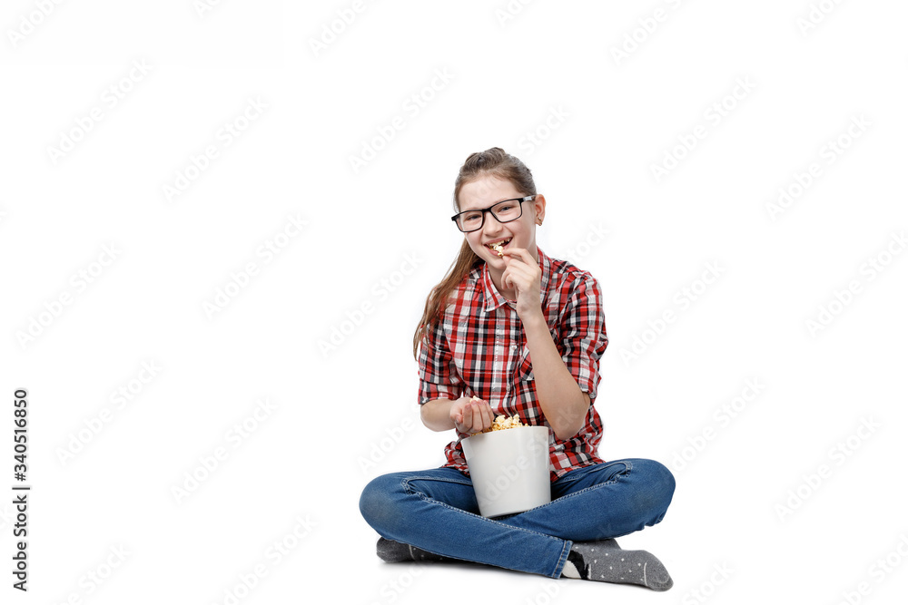 Cheerful girl in glasses with a bucket of popcorn in his hands eats it with an appetite on a white background
