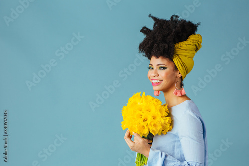 Portrait of a very happy young woman in blue holding bouquet of fresh yellow daffodils looking to side photo