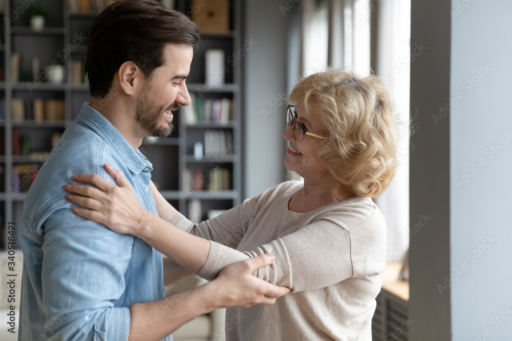 Obraz premium Elderly mother admires matured adult son looking at him smiles enjoy long awaited meeting after separation feels happy and proud, side view. Loving grown up child visited mom, familial ties concept