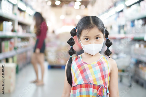Asian child or kid girl wear N95 face mask for close mouth nose and cold cough sick to protect influenza virus covid-19 or PM2.5 dust smoke and bacteria for shopping in department store or supermarket