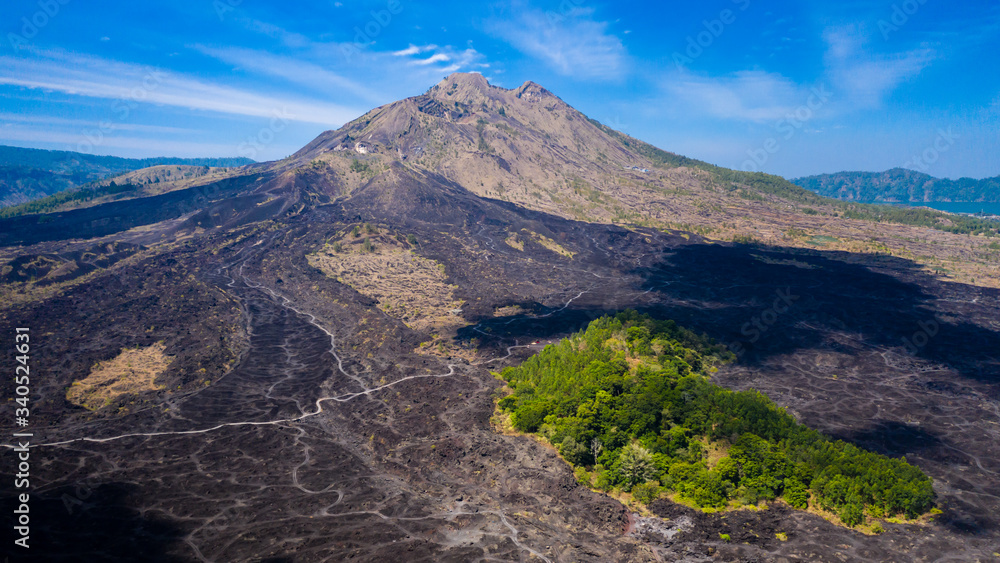 Aerial view of a tiny island of green surrounded by black, solidified lava flows around an active volcano (Mount Batur)