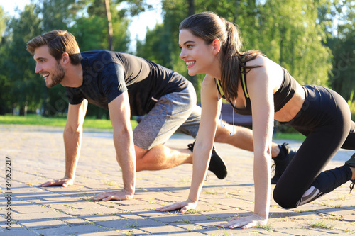 Young couple doing exercise together while working out outdoors in park.