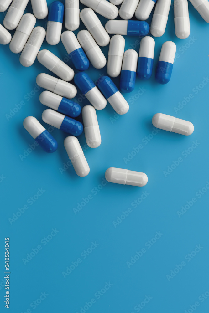 Blue and white medicine capsules on blue background with copy space. Pile of scattered capsules. Antivirus pharmacy. Pharmaceutical theme. Blue and white medicine capsules on blue background with copy space. Pile of scattered capsules. Antivirus pharmacy. Pharmaceutical theme.