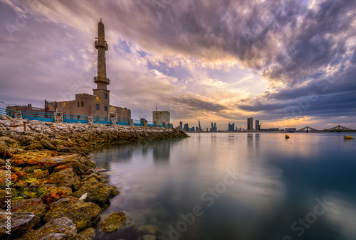 Beautiful view of Hanan Ali Kanoo Mosque in Al Ghous park and Manama city at the background with striking clouds during sunset.