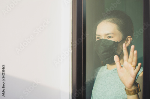 Asian girl wearing a medical mask for against infection and prevent spread of Coronavirus,She touches her hand in the glass window,Covid-19.
