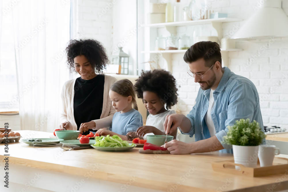 Happy young multiethnic family with little daughters have fun cooking at home together, smiling parents and small multiracial children prepare breakfast salad in kitchen, healthy lifestyle concept Happy young multiethnic family with little daughters have fun cooking at home together, smiling parents and small multiracial children prepare breakfast salad in kitchen, healthy lifestyle concept